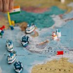 Mapa-múndi com pequenos navios e bandeiras indicando rotas e pontos do comércio internacional