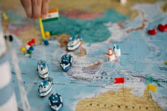 Mapa-múndi com pequenos navios e bandeiras indicando rotas e pontos do comércio internacional
