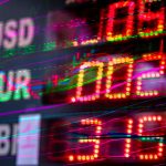 Painel eletrônico exibe cotações e variações de moedas como dólar, euro e libra em um ambiente de mercado financeiro.