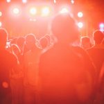 Público reunido em um festival de música ao ar livre, diante de um palco iluminado.